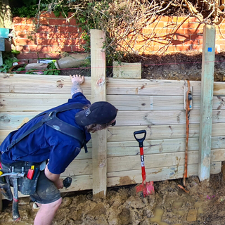 Builder inspecting work being done on wooden retaining wall