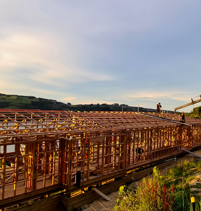 View of house framing as builders work with harbour in the background