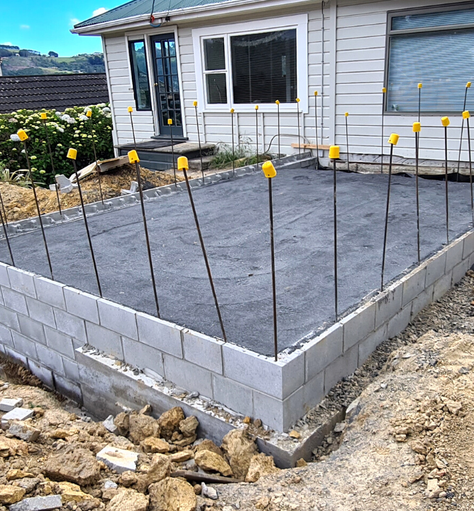 weatherboard house being extended with cinderblock and pad area marked ready for framing