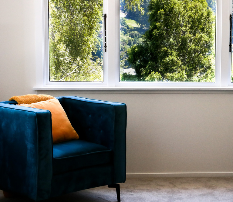 Single blue velvet armchair in a newly renovated room with wide windows overlooking treetop view