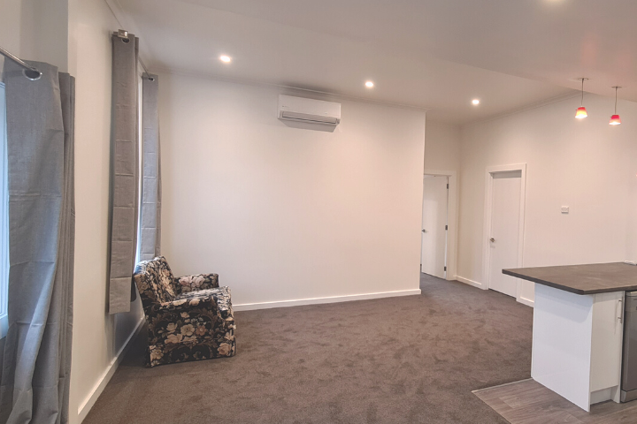 Recently renovated lounge and kitchen with new grey carpet, updated paint and curtains, and armchair