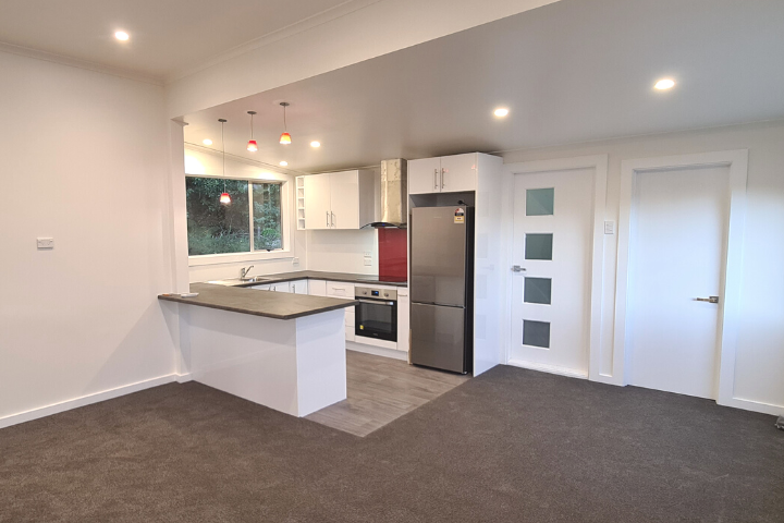 Kitchen and lounge area in a newly renovated house with fridge and red splashback