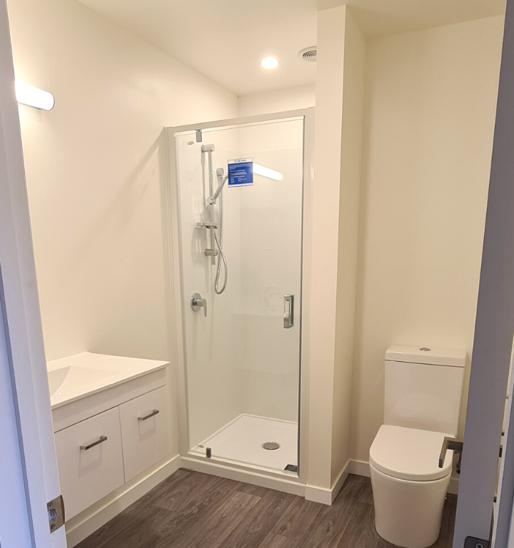 Vanity, shower cubicle and toilet in newly renovated bathroom, with wooden floors and white walls